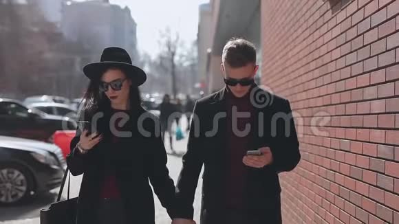时尚情侣们低头看着他们的智能手机沿着城市街道走着视频的预览图