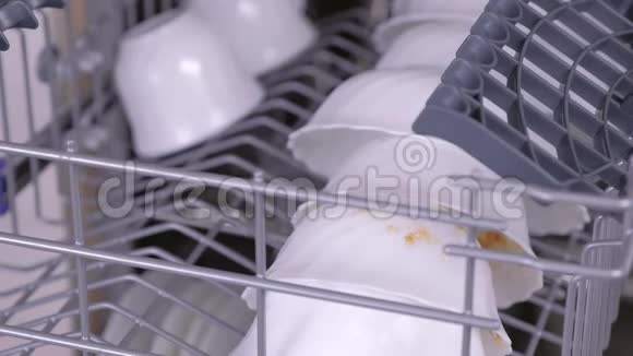 男人手放着白色的脏杯和玻璃用脏的白色盘子关上洗碗机视频的预览图