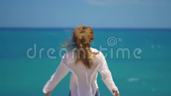 在美丽的海面上年轻女子的头发随风飘动双手举在悬崖之上概念自由视频的预览图