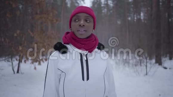 美国黑人女孩走在冬天的森林里环顾四周她挺直了围巾穿暖和夹克的漂亮女孩视频的预览图