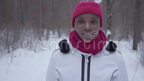 肖像自信成功的年轻微笑的非裔美国女孩穿着温暖的戴着红帽子围巾和白色夹克视频的预览图
