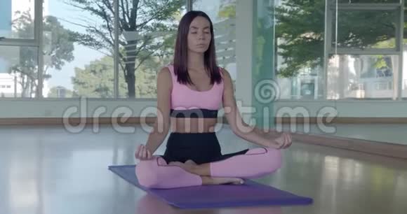 漂亮的女人在有玻璃墙的健身房地板上做瑜伽运动冥想视频的预览图