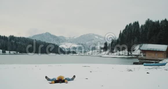 在白雪皑皑的湖山中有一个大森林游客兴高采烈地躺在雪地上然后跳起来视频的预览图