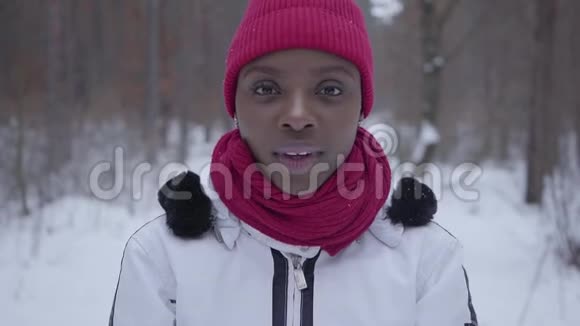 非洲裔美国女孩的肖像抛了一把雪站在冬天的森林和看镜头美丽美丽视频的预览图