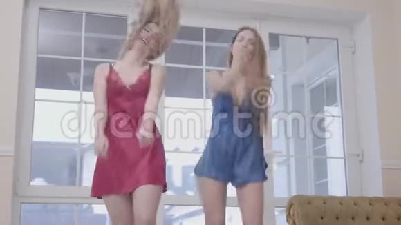 早上两个漂亮漂亮的年轻女孩在大的落地窗附近的现代客厅里跳舞视频的预览图