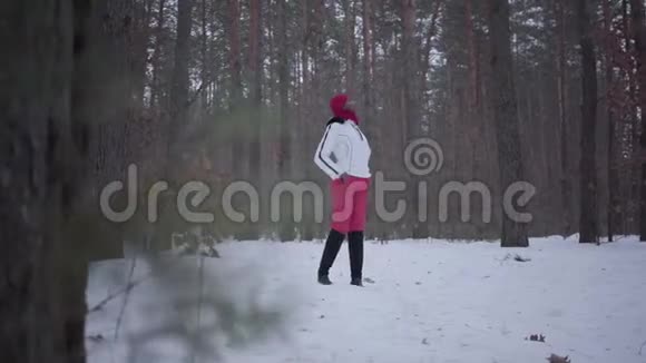 迷路的非裔美国女孩穿着温暖的衣服戴着红色的帽子围巾和白色的夹克站在冬天的森林里视频的预览图