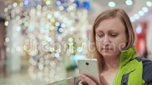 一个女人惊讶地看着智能手机站在购物中心背景是一个灯泡视频的预览图