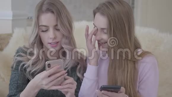 两个漂亮的年轻女朋友坐在客厅的沙发上寻找购物的好折扣视频的预览图