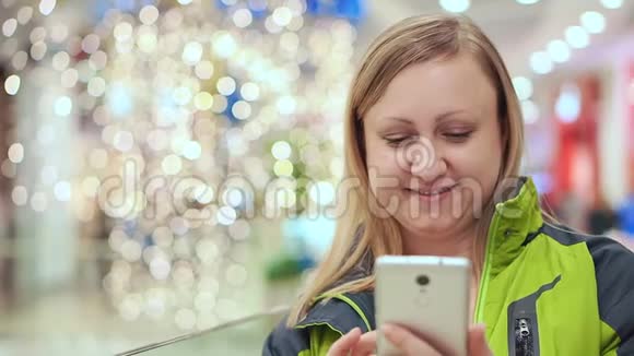 一个女人正在看一条智能手机信息微笑着站在一个购物中心背景是视频的预览图