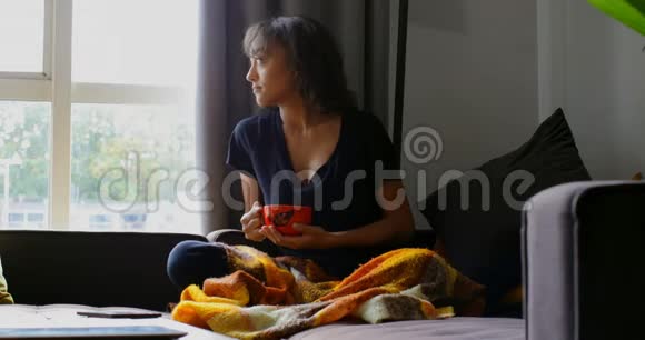 亚洲年轻女子在家客厅喝咖啡的正面景色视频的预览图