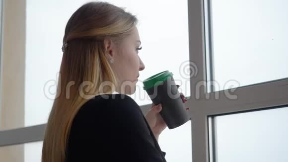商务女性从杯子里喝咖啡在办公室里寻找窗口视频的预览图