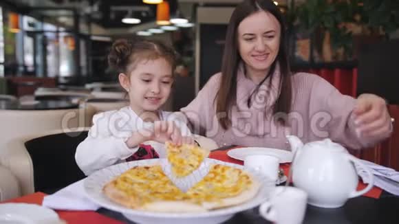 女人和小女儿在一家餐馆里只吃煮熟的奶酪披萨妈妈把茶倒进杯里视频的预览图