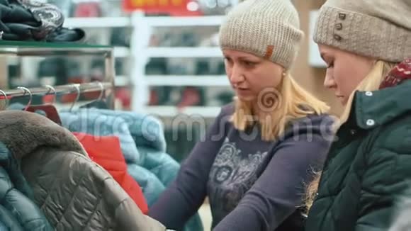 漂亮的女人和她的女儿正在服装店里挑选一件新的羽绒服视频的预览图