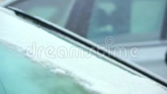 一个年轻的女孩用绿色的刷子把她的汽车的玻璃从雪地上擦干净冬天的早晨视频的预览图