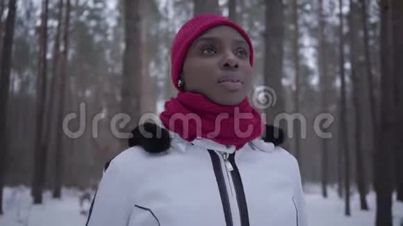 美国黑人女孩站在冬天的森林里看上去笔直穿暖和夹克的漂亮女孩在户外视频的预览图