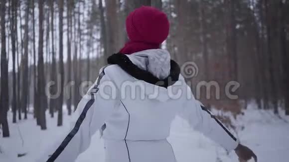 非裔美国女孩在冬天的森林里四处张望穿暖和夹克的漂亮女孩张开双臂拥抱视频的预览图