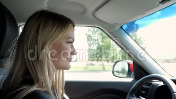 金发的年轻女子正在城市里驾驶一辆汽车手握方向盘视频的预览图