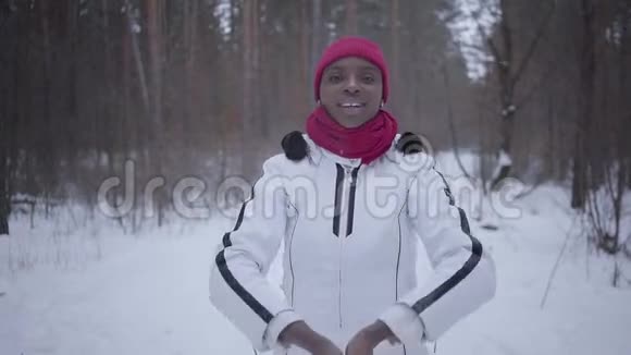 非洲裔美国女孩扔出一把雪站在冬季森林和看镜头可爱的女孩视频的预览图