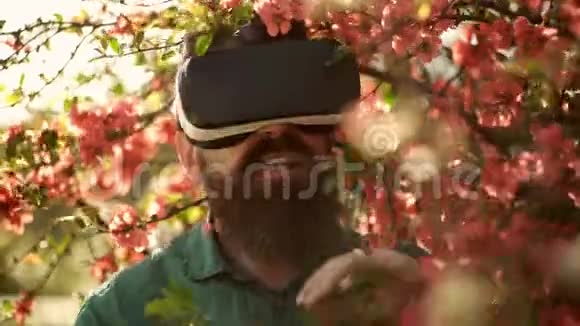 春天花园里留胡子的男人戴着虚拟现实眼镜大胡子男人用小玩意探索环境带移动设备的Hipster视频的预览图