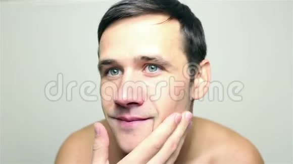 年轻的帅哥刮胡子后用手微笑和触摸他的脸视频的预览图