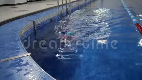 穿着泳衣帽子和护目镜的小女孩正在潜水和游泳到游泳池视频的预览图