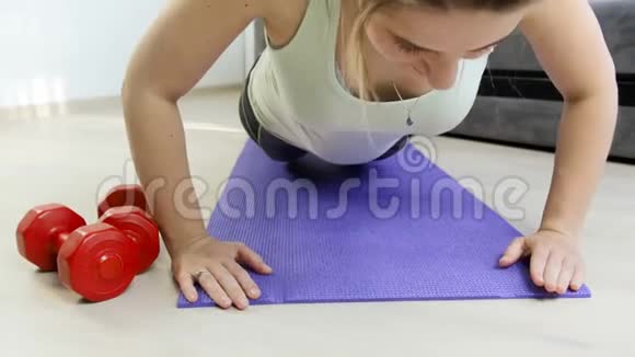4K录像显示年轻运动女子在客厅地板上做俯卧撑在家锻炼身体视频的预览图