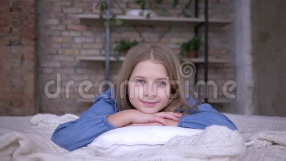 快乐的童年美丽的小女孩的肖像蓝眼睛躺在床上的枕头上视频的预览图
