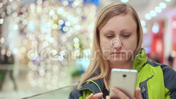一个女人正在读一条智能手机信息感到心烦意乱她站在一个购物中心里面有一个灯泡视频的预览图