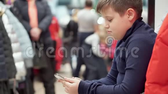 一个男孩在服装店里坐着等着他的母亲视频的预览图