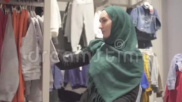 穆斯林妇女戴着头巾和背包在购物中心儿童商店里挑选衣服视频的预览图