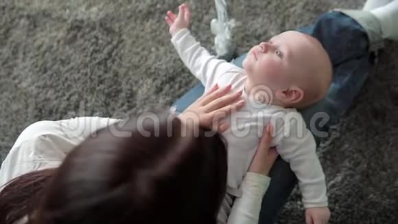 一位美丽的母亲和婴儿在地板上微笑的特写肖像视频的预览图