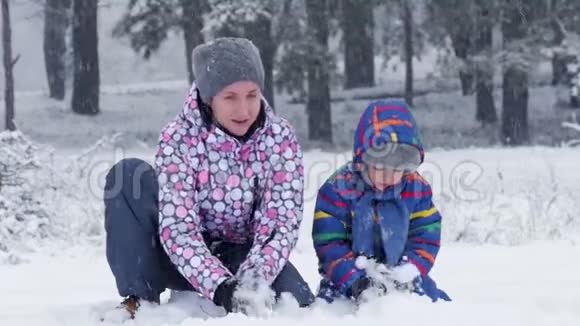 快乐的妈妈和她的儿子向相机扔雪在美丽的冬日雪天森林或公园里的幸福家庭视频的预览图