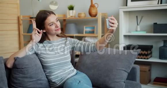 迷人的女孩在沙发上用智能手机相机自拍摆姿势视频的预览图