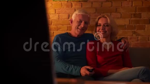 在舒适的室内沙发上一对幸福的老夫妇在看电视节目时兴奋地笑着视频的预览图
