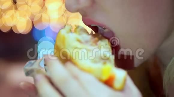 一个年轻的少女在咖啡馆里咬着一个美味的汉堡包快餐晚上在灯光的背景下视频的预览图