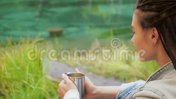 女徒步旅行者坐在绿草地上喝茶视频的预览图