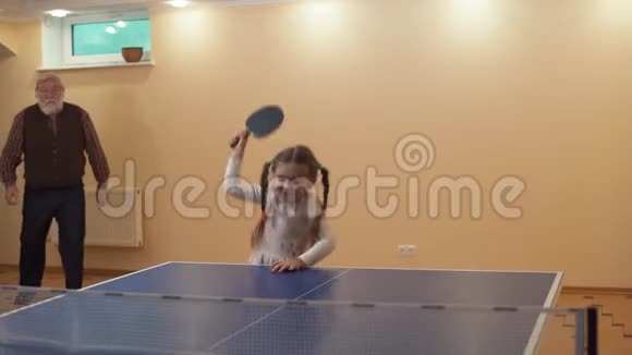 小女孩在网球桌附近跳跃手里拿着火箭爷爷来拿球拍快乐家庭游戏视频的预览图