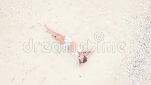 微笑的女人躺在白色的沙滩上在海滩上鸟瞰在度假海滩上放松身心的年轻黑发女人视频的预览图