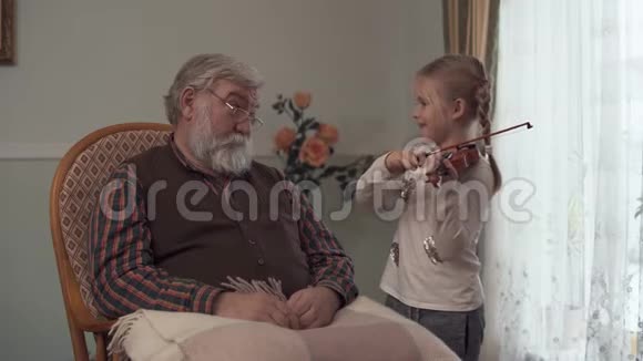 祖父坐在摇椅上他那滑稽的孙女轻轻地抚摸着小提琴拉得不好视频的预览图
