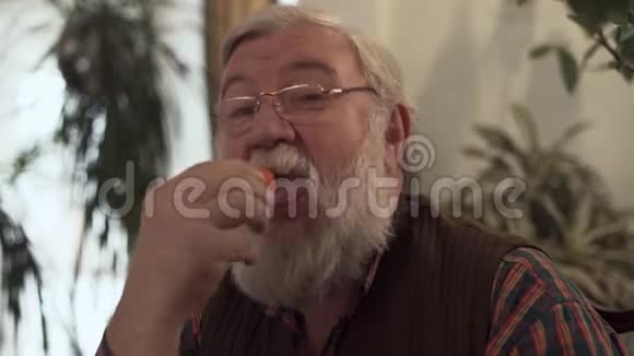大胡子男人坐在家里吃樱桃然后露出大手指成熟的男人引领健康的生活方式住宅植物视频的预览图