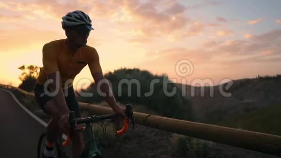 骑自行车的人穿着黄色t恤在公路上日落时分骑着山地车视频的预览图