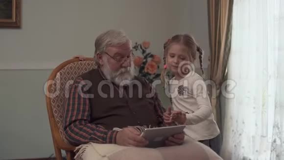 大胡子老人坐在摇椅上手里拿着平板电脑两个小女孩站在爷爷旁边看着视频的预览图