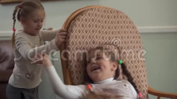 小女孩在一把摇椅上摇晃着妹妹两个扎着辫子的可爱女孩在家玩得很开心视频的预览图