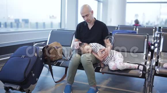 一个无聊的男人在屁股机场等着怀里抱着一个疲惫的小女儿等待着登机的开始视频的预览图