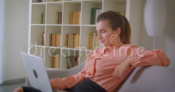 年轻漂亮的女商人在笔记本电脑上工作看着相机兴高采烈地坐在上面微笑视频的预览图