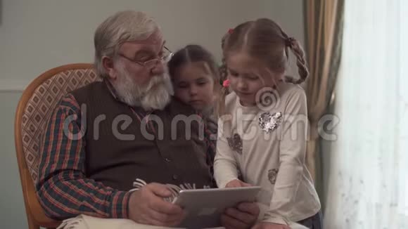 祖父给他的两个可爱的孙女看了平板电脑上的东西拿着一个格子在摇椅上摇摆视频的预览图