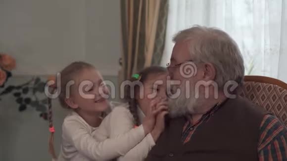 两个可爱的女孩和他们的祖父坐在椅子上玩孙女们刮胡子长得像个老男人视频的预览图