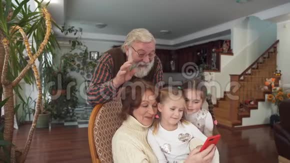 成熟的夫妇和他们的孙子用手机用相机说话女人坐在滚动的椅子上老人和女孩视频的预览图