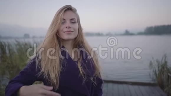 一个年轻的女人在码头边湖的背景下呼唤着她视频的预览图