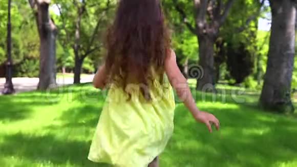 快乐的小女孩穿着黄色连衣裙光着脚在公园的绿草上奔跑视频的预览图